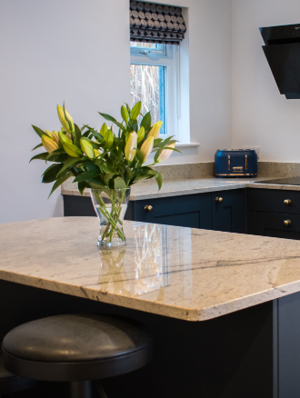 Wide view of an Ivory Spice Granite island worktop with breakfast bar seating, showing the island shape, dark cabinetry and light Granite surface.
