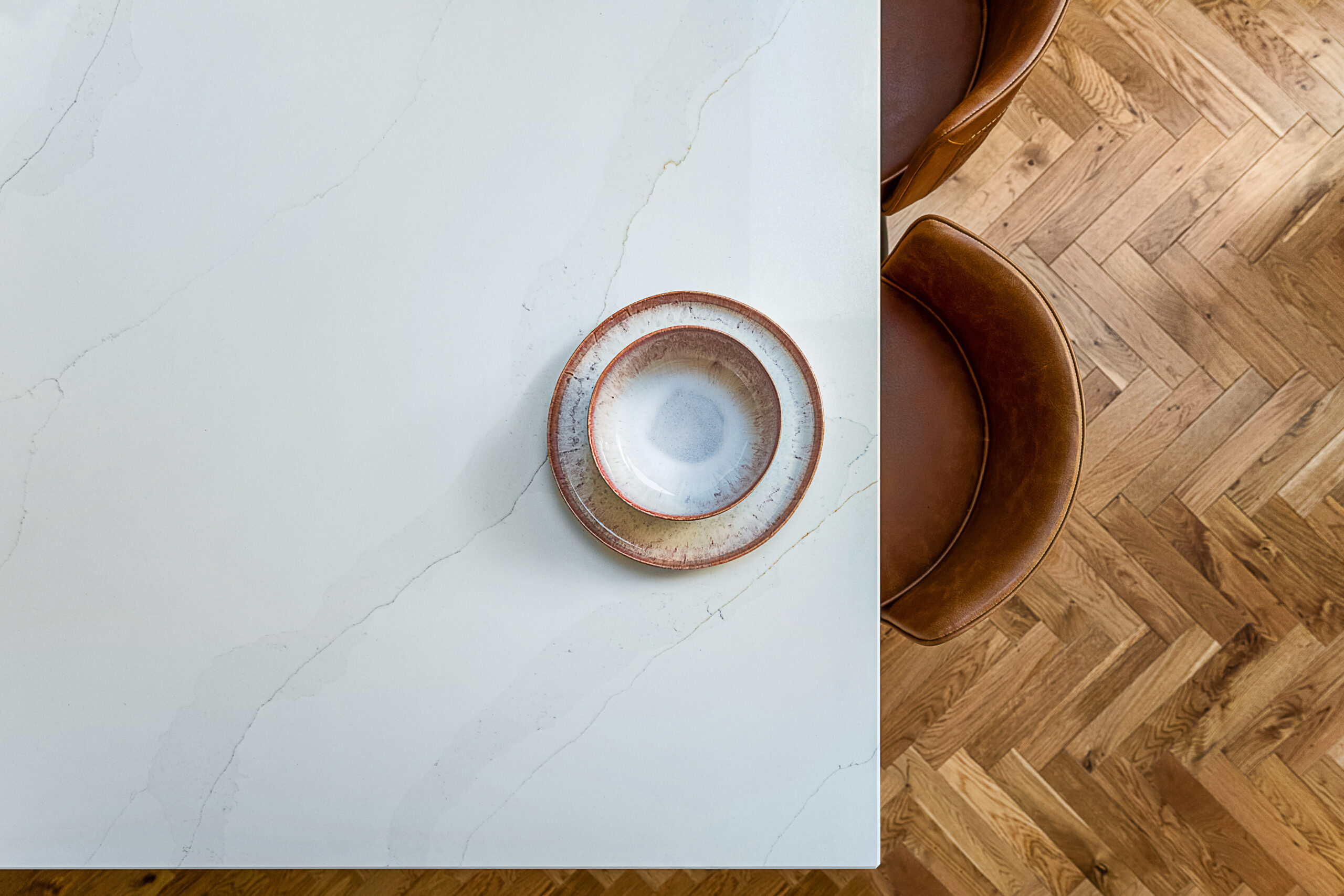 Top down view of Eternal Calacatta Quartz worktop with ceramic plates and warm toned chairs