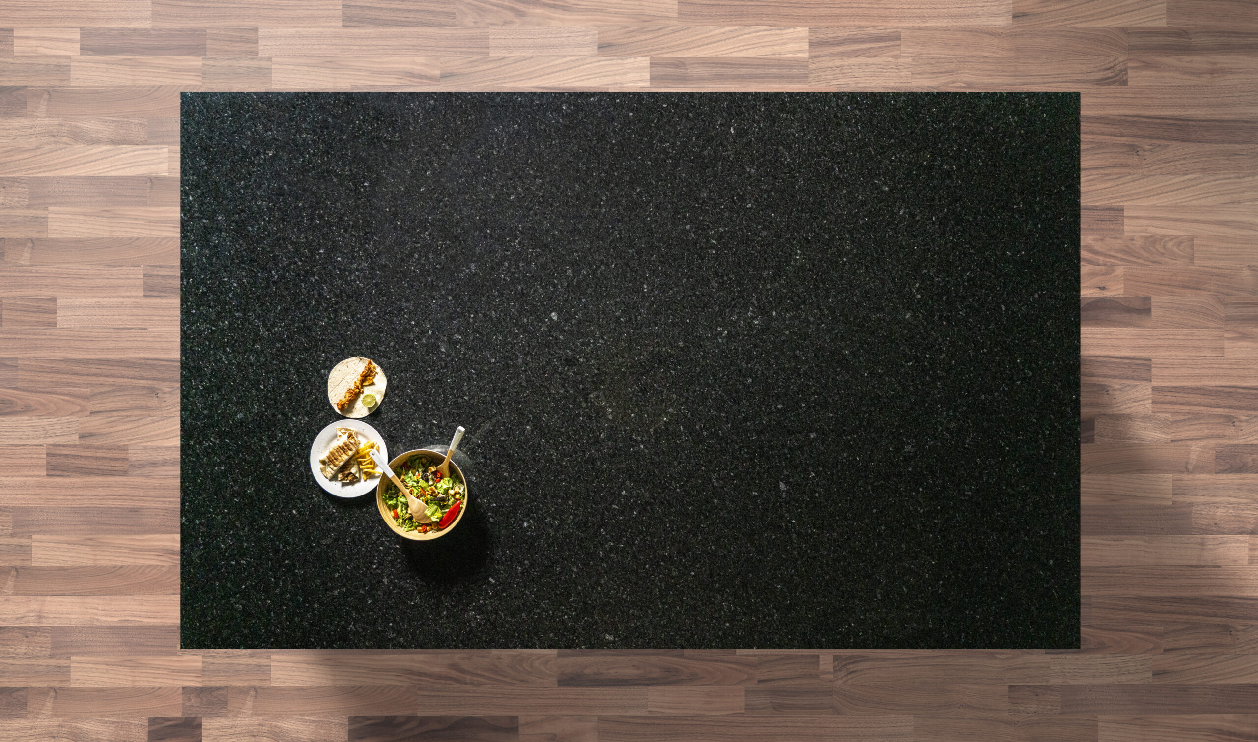 Overhead view of an Angola Black Granite worktop showing a dark speckled pattern, photographed from above with a small styled tray in the corner.