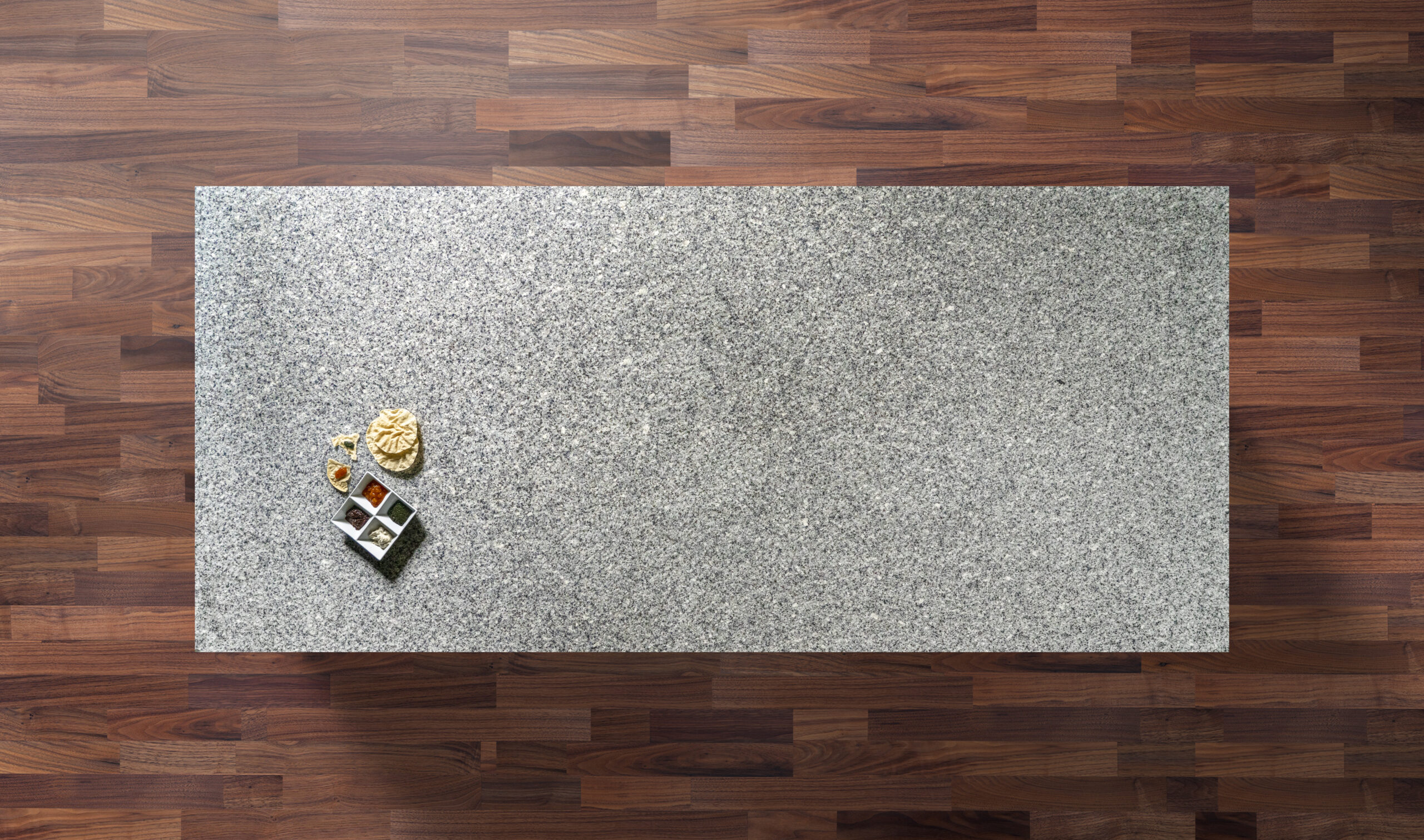 Overhead view of an Azul Platino Granite worktop showing a light grey speckled pattern, photographed from above with a small styled tray in the corner.