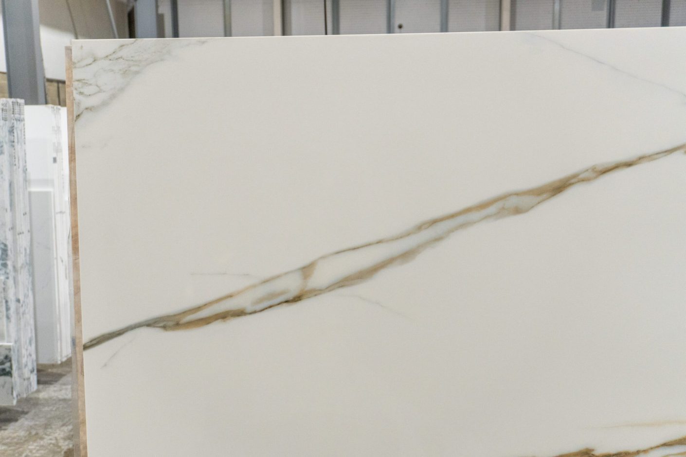 Calacatta Vagli Gold Porcelain slab section with a long flowing gold vein across a white background