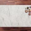 Carrara Venato Gold Porcelain worktop surface in soft white with light grey veining and warm gold toned accents, photographed from above with small bowls