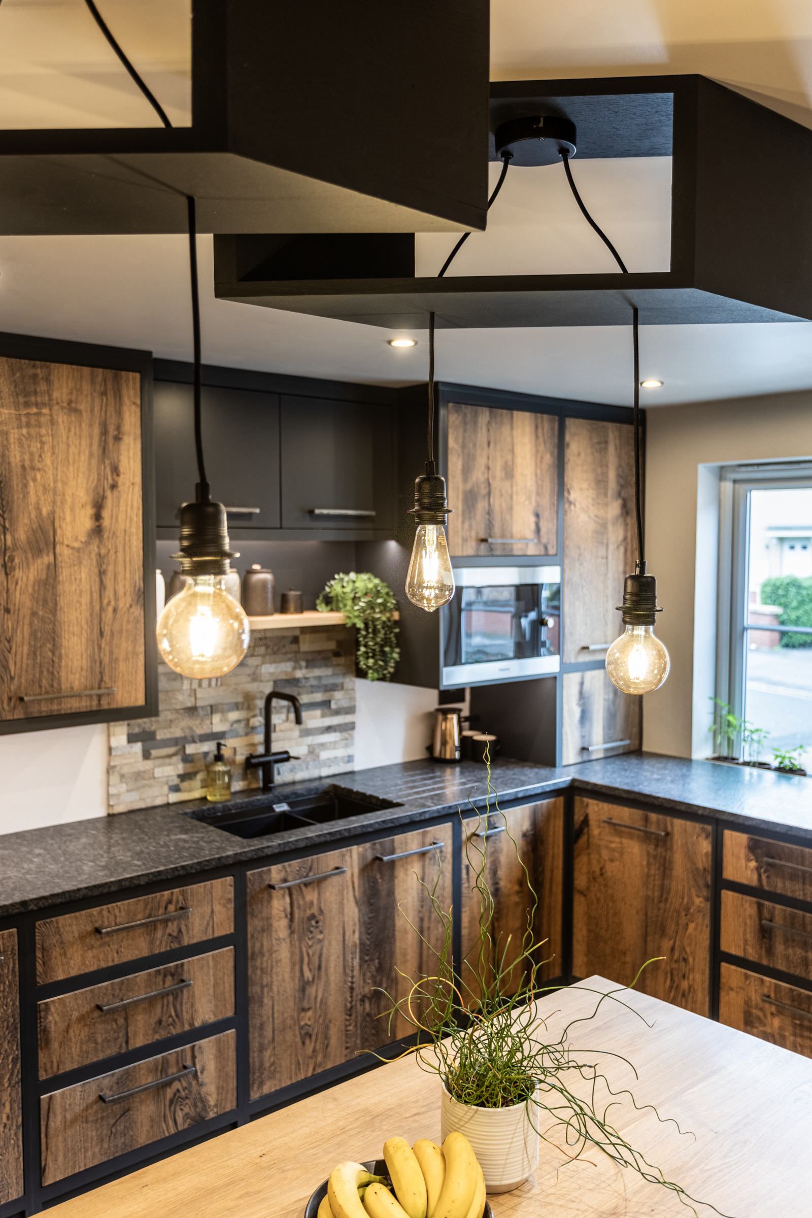 Corner kitchen view with Steel Grey leather Granite worktops and matching splashback detail, shown with rustic wood cabinetry and pendant lights above the worktop.