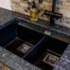 Close up of an undermount double bowl sink set into Steel Grey leather Granite worktop, showing the textured finish and clean cut-out lines.
