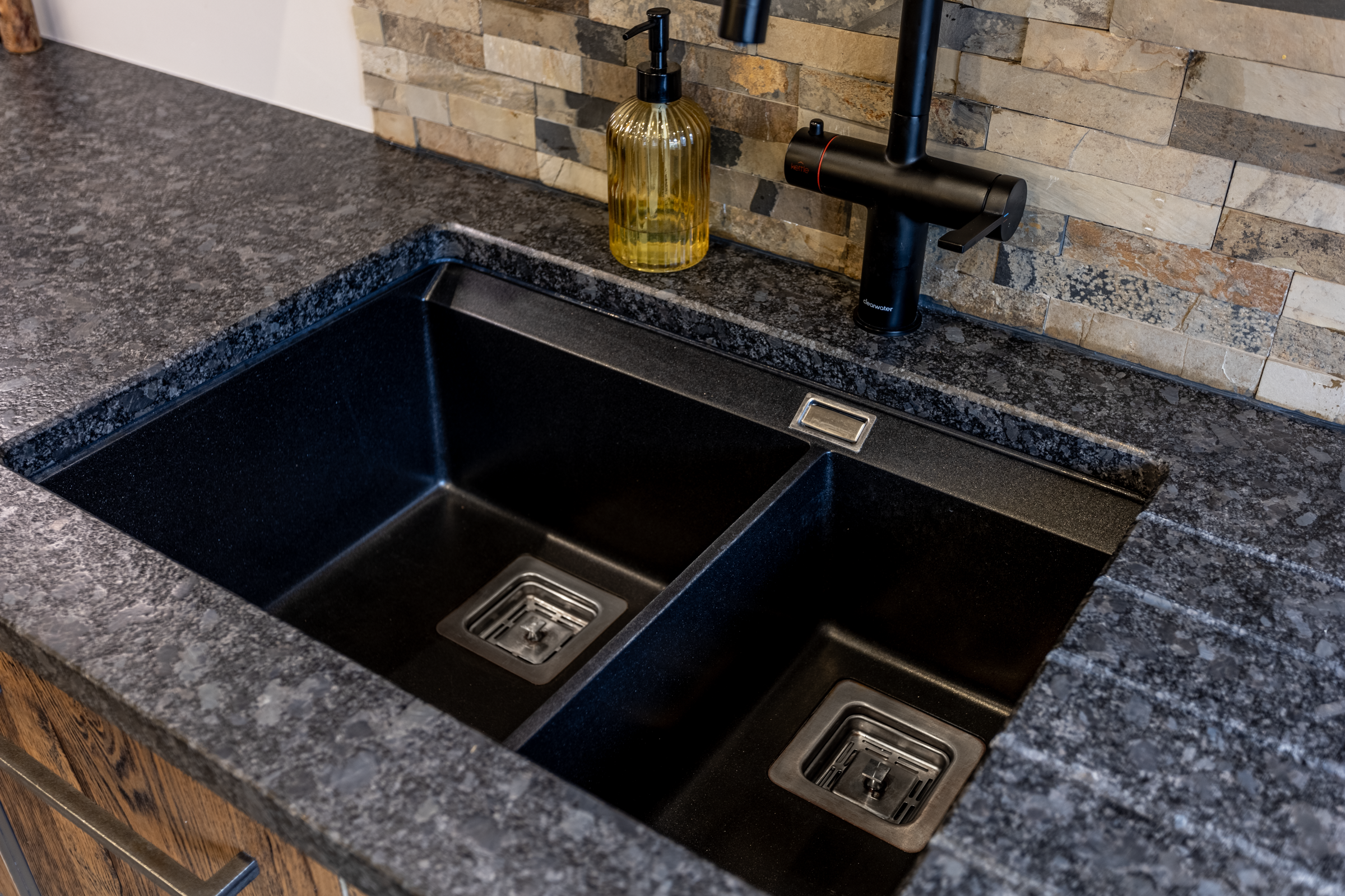 Close up of an undermount double bowl sink set into Steel Grey leather Granite worktop, showing the textured finish and clean cut-out lines.