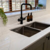 White Macaubus Quartz worktop with an undermount sink and black tap, showing subtle grey veining