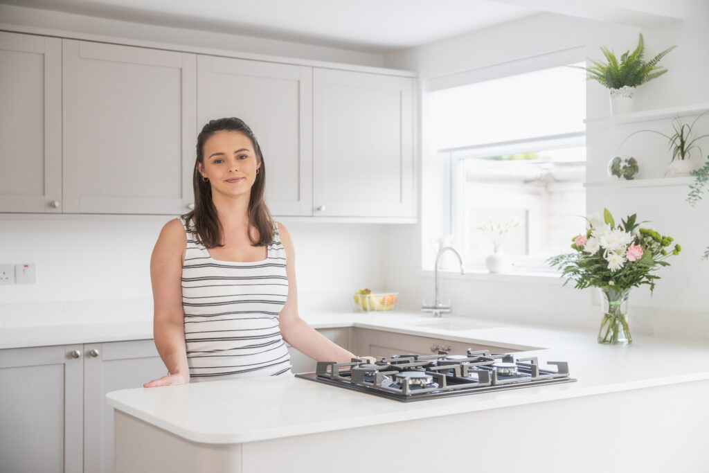 Megan customer testimonial image in her kitchen with Bluetta Carrara Quartz worktops visible around the hob