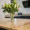 Close up of an Ivory Spice Granite island worktop with a vase of flowers, showing warm cream tones, soft veining and a polished reflective finish.