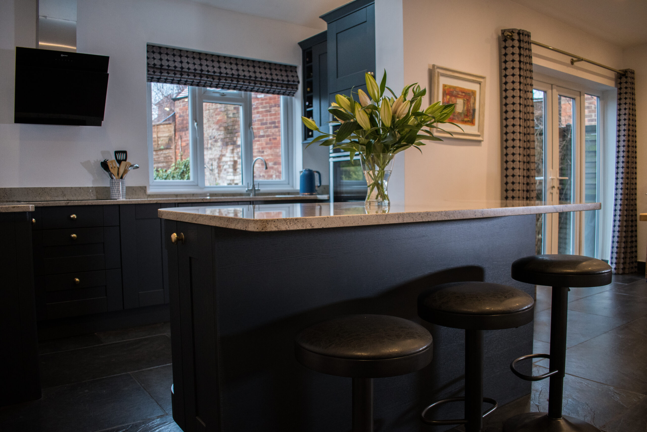 Open plan kitchen view showing an Ivory Spice Granite island with breakfast bar seating, with windows behind and the Granite surface catching the light.