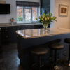Angled view of an Ivory Spice Granite island worktop with breakfast bar stools, showing the polished Granite finish and clean edge detail in a dark kitchen.