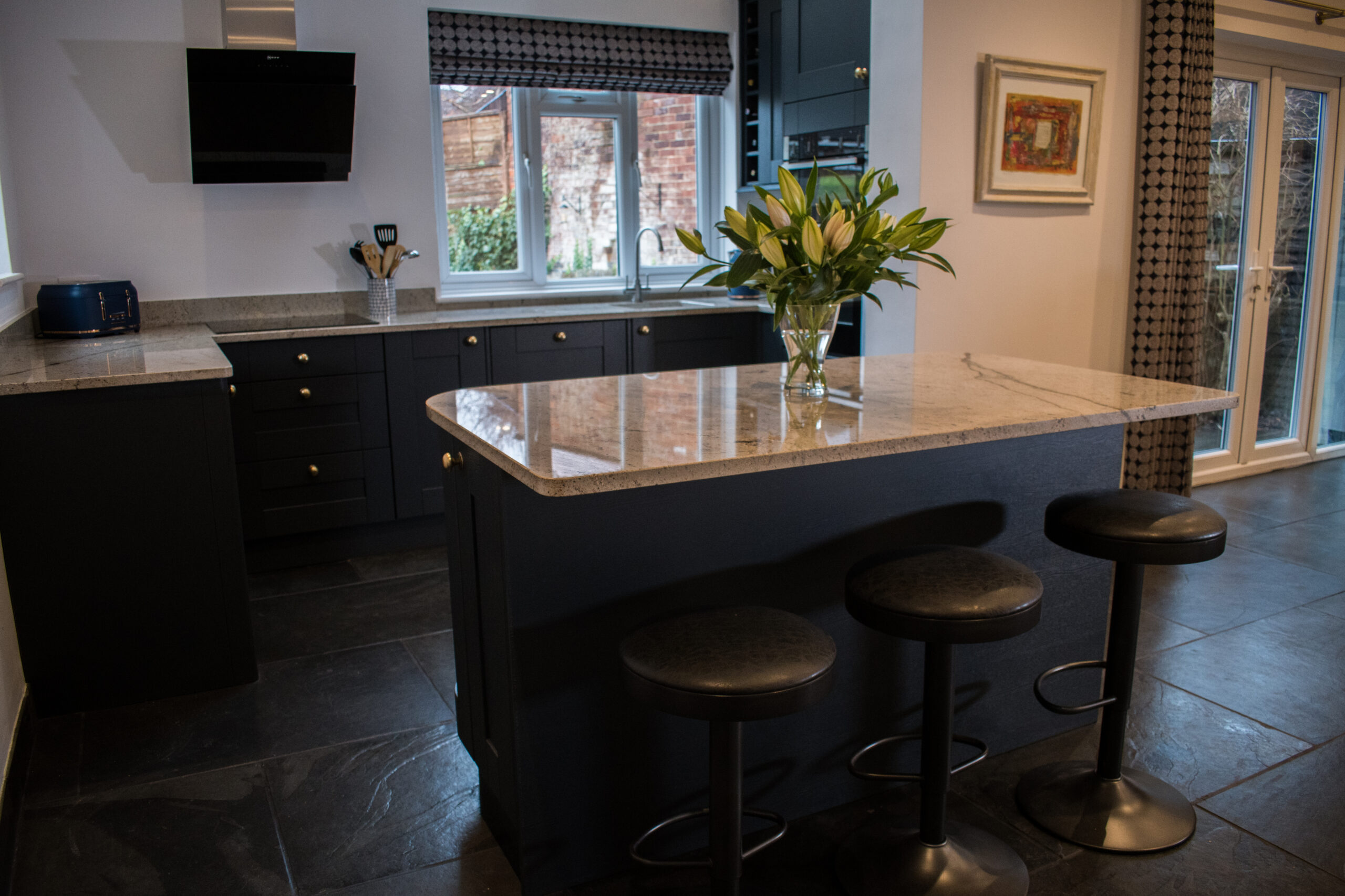 Angled view of an Ivory Spice Granite island worktop with breakfast bar stools, showing the polished Granite finish and clean edge detail in a dark kitchen.