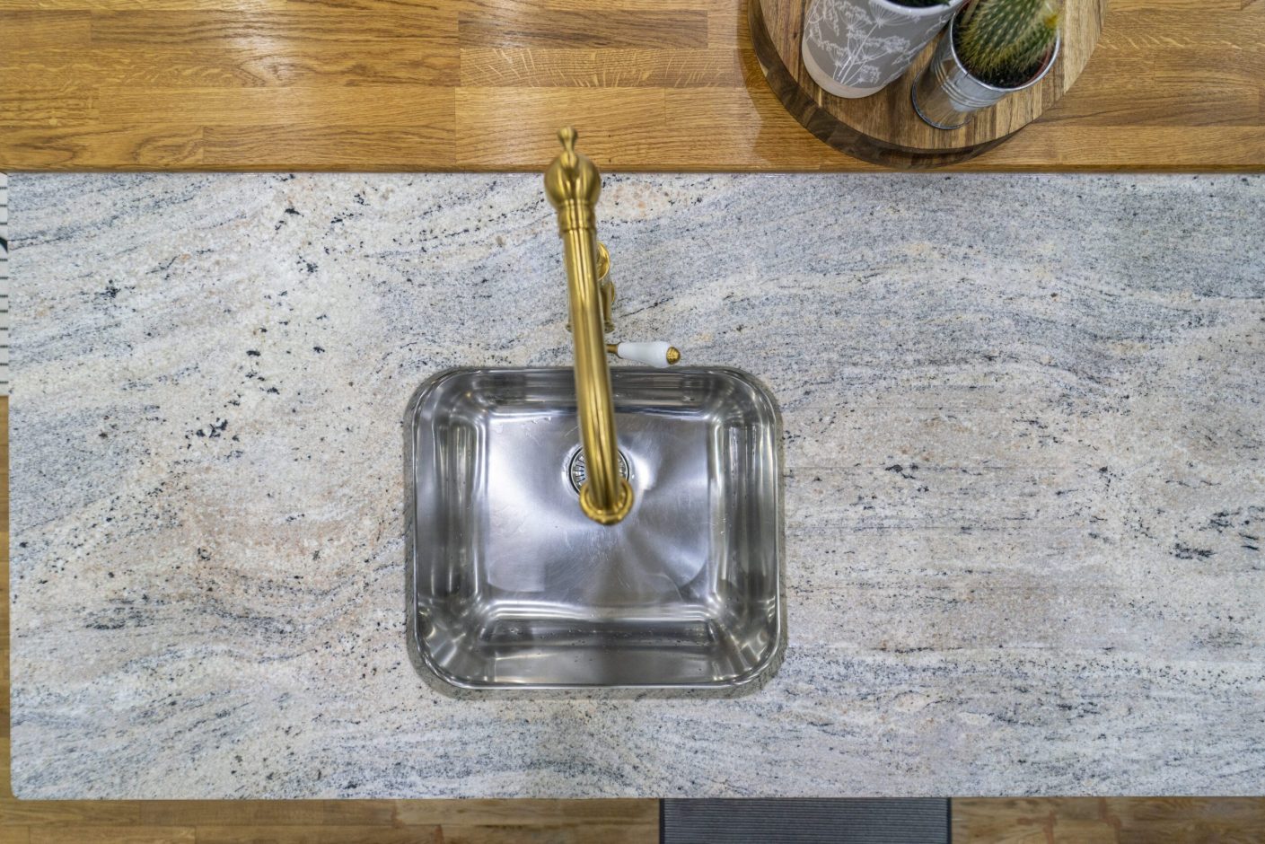 Overhead view of a square inset sink and brass tap set into Ivory Fantasy Granite worktop, showing the Granite pattern and clean cut-out lines.
