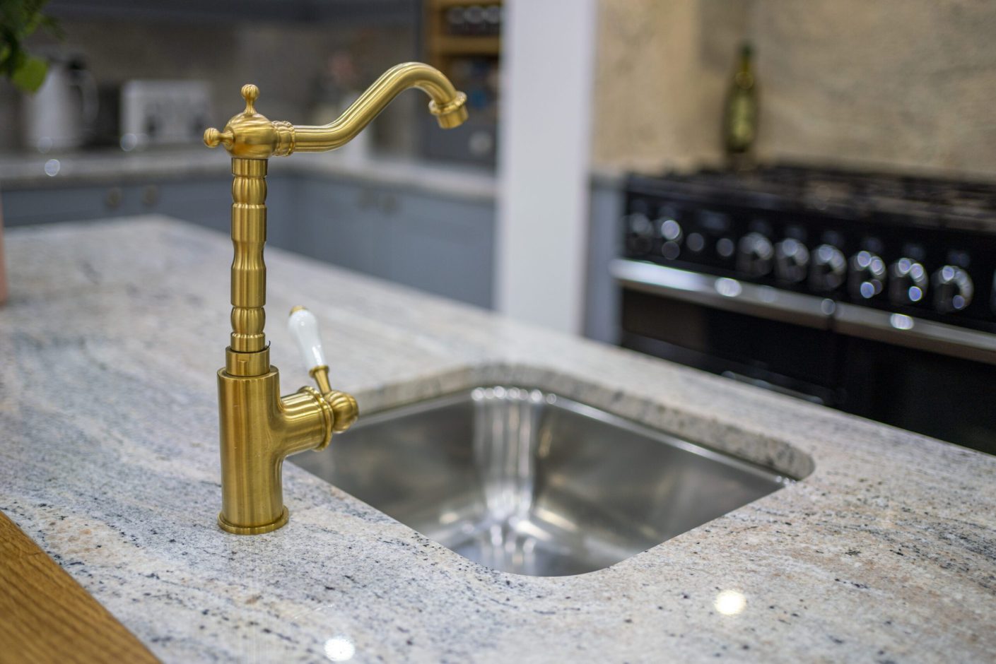 Close up of an inset stainless steel sink in Ivory Fantasy Granite with a brass tap, showing the polished Granite surface around the cut-out.