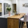 Kitchen island end view with Ivory Fantasy Granite worktop and inset sink, showing waterfall end panel, bar stools and flowers on the island.
