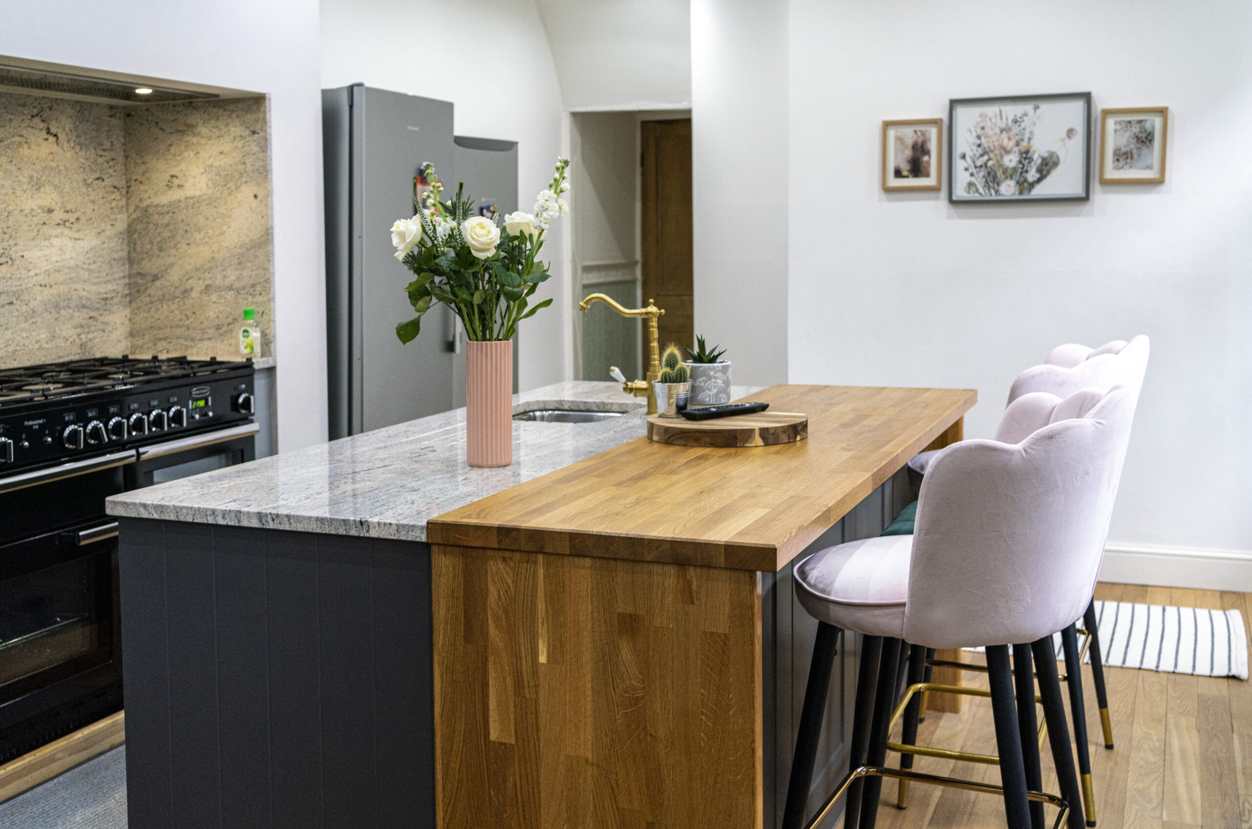 Kitchen island end view with Ivory Fantasy Granite worktop and inset sink, showing waterfall end panel, bar stools and flowers on the island.