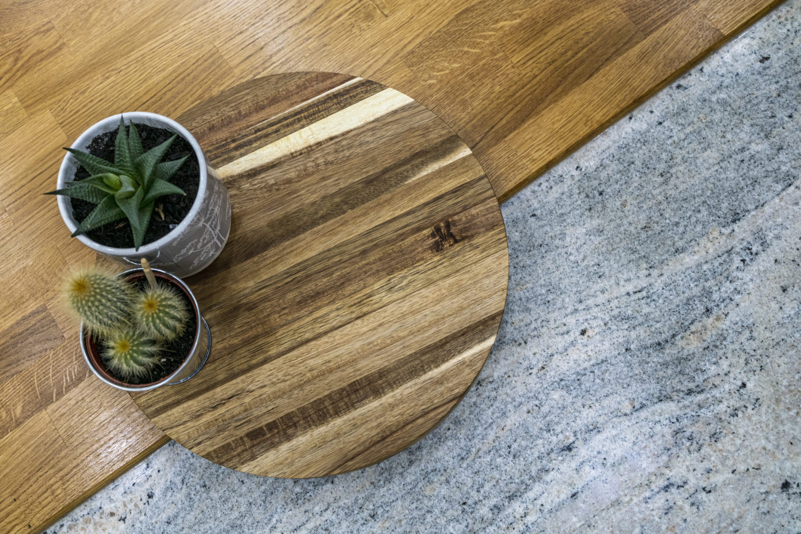 Styled close up of Ivory Fantasy Granite worktop with a round wooden board and small plants, showing the Granite colour, speckling and surface finish.