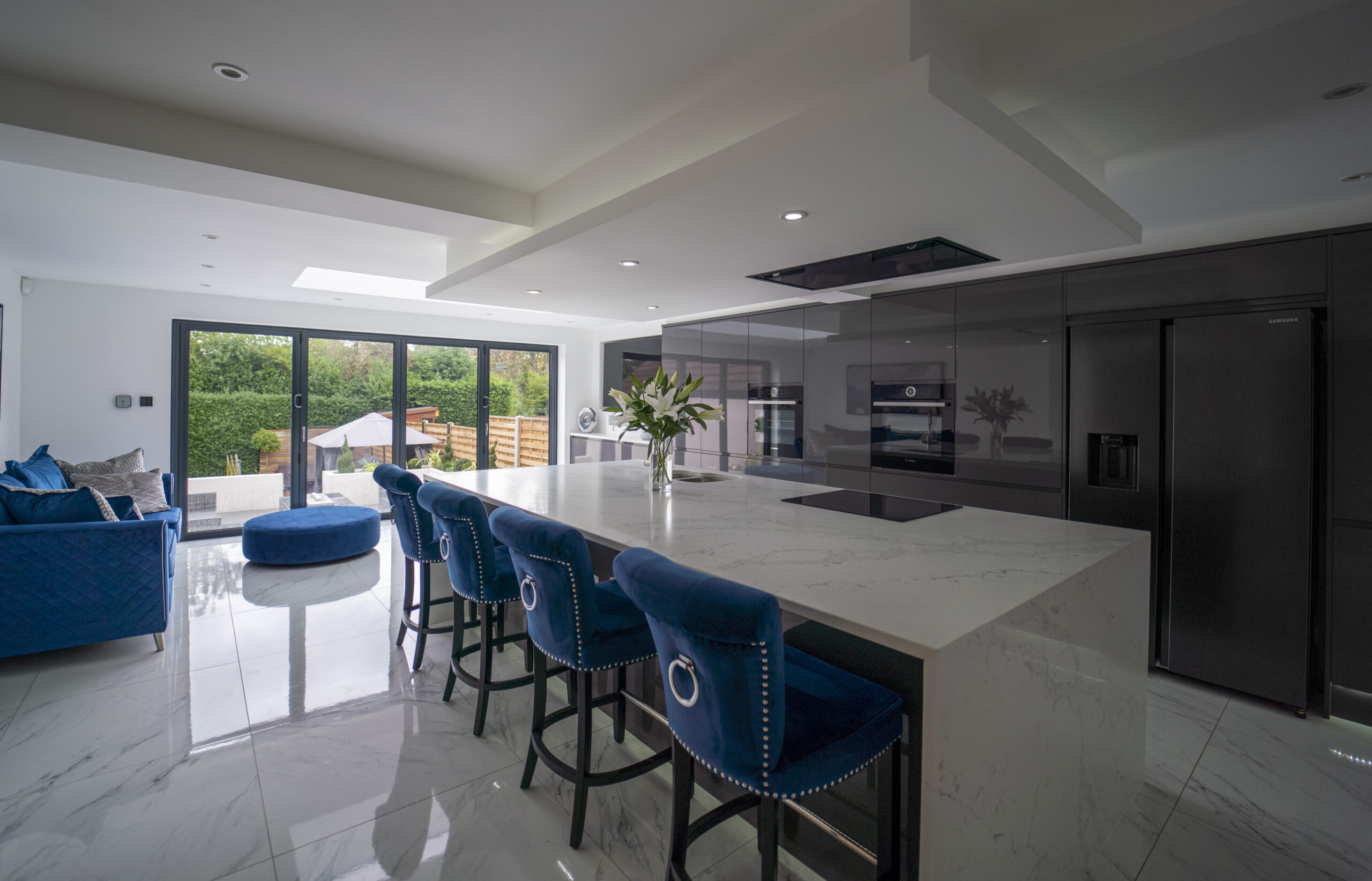 Modern open plan kitchen with White Calacatta Quartz island and blue bar stools under skylights