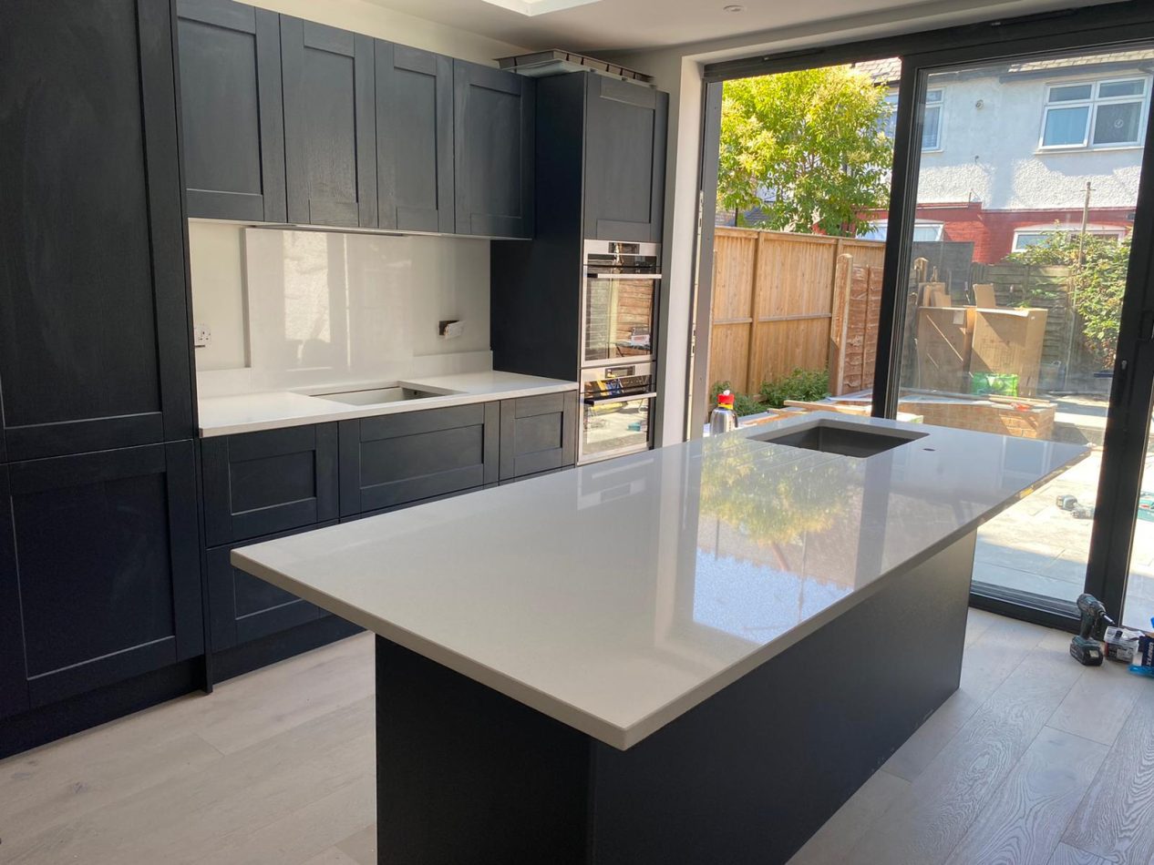 Stardust Quartz island worktop with glossy white surface in a modern kitchen with dark cabinetry and large patio doors