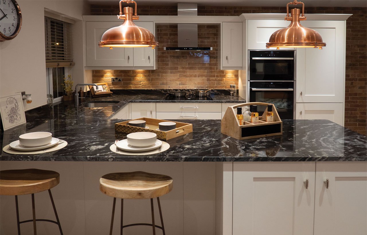 Modern kitchen island with Black Storm Granite worktop, showing dramatic veining under pendant lights with bar stools and place settings.
