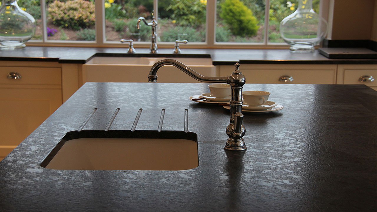 Sink area in Steel Grey leather Granite with drainer grooves and an inset sink, showing the textured finish around a chrome tap by the window.