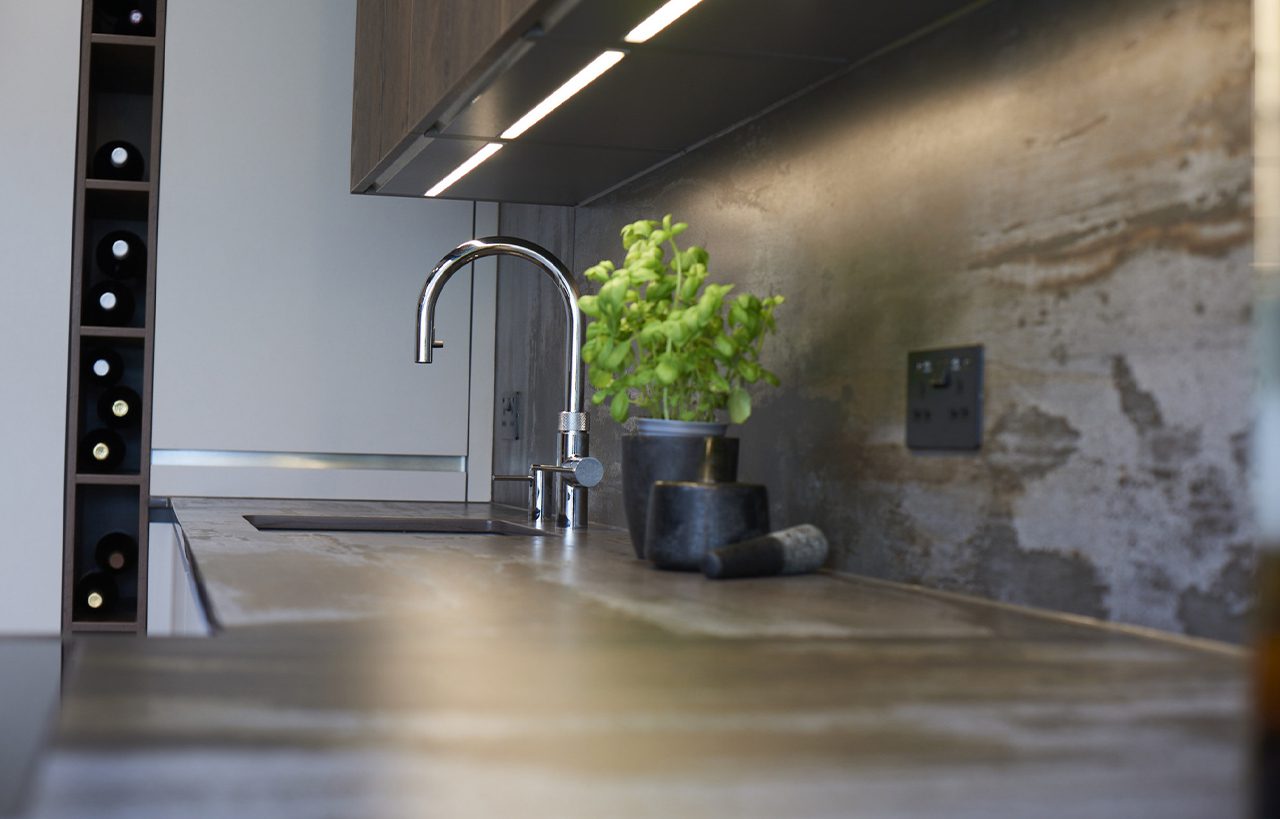Trilium Porcelain worktop with matching splashback, chrome tap, and a small green plant beside the sink area in a modern kitchen