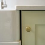 Close up of Carrara Quartz worktop around white inset sink with brass knob cabinetry
