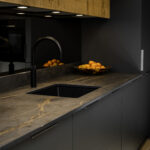 Laurent Porcelain worktop with gold veining installed around an undermount sink and black tap, with fruit bowl on the surface.