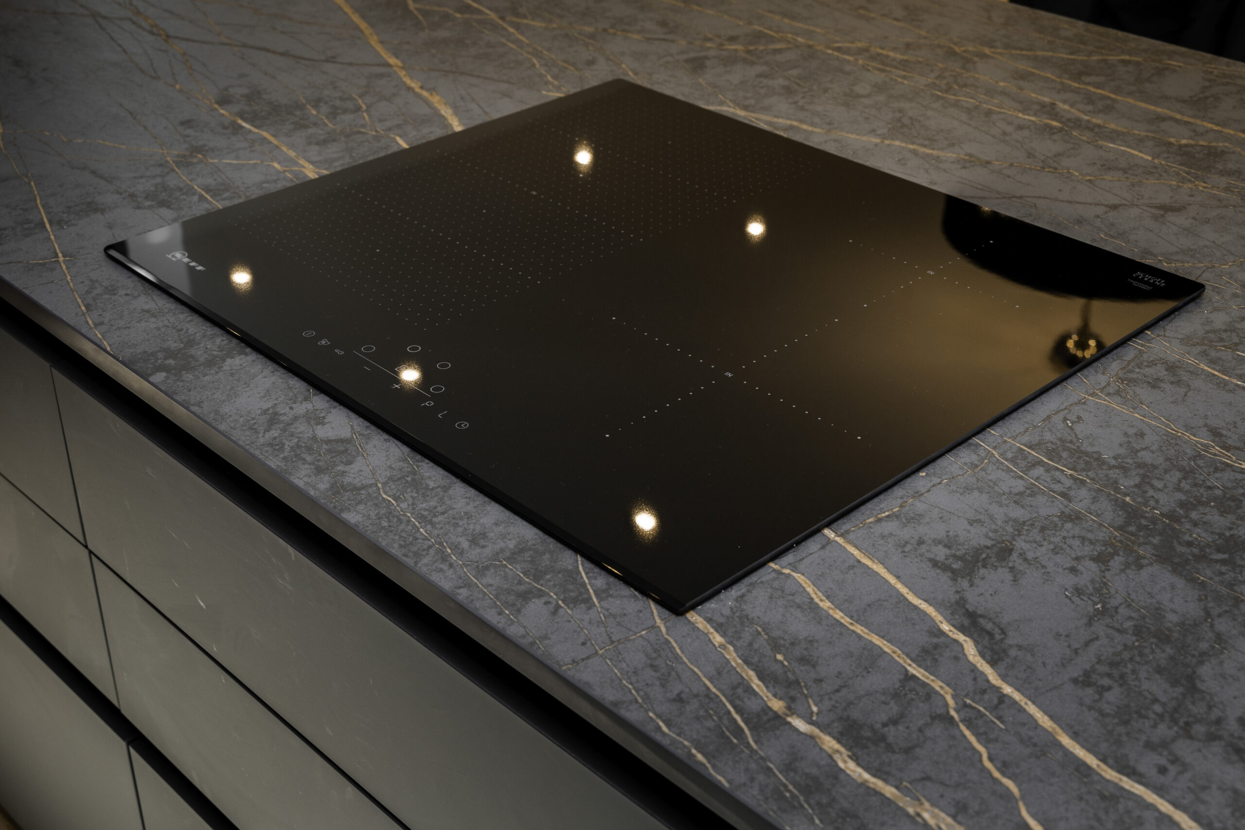 Close-up of a flush black induction hob set into a Laurent Porcelain worktop with gold veining.