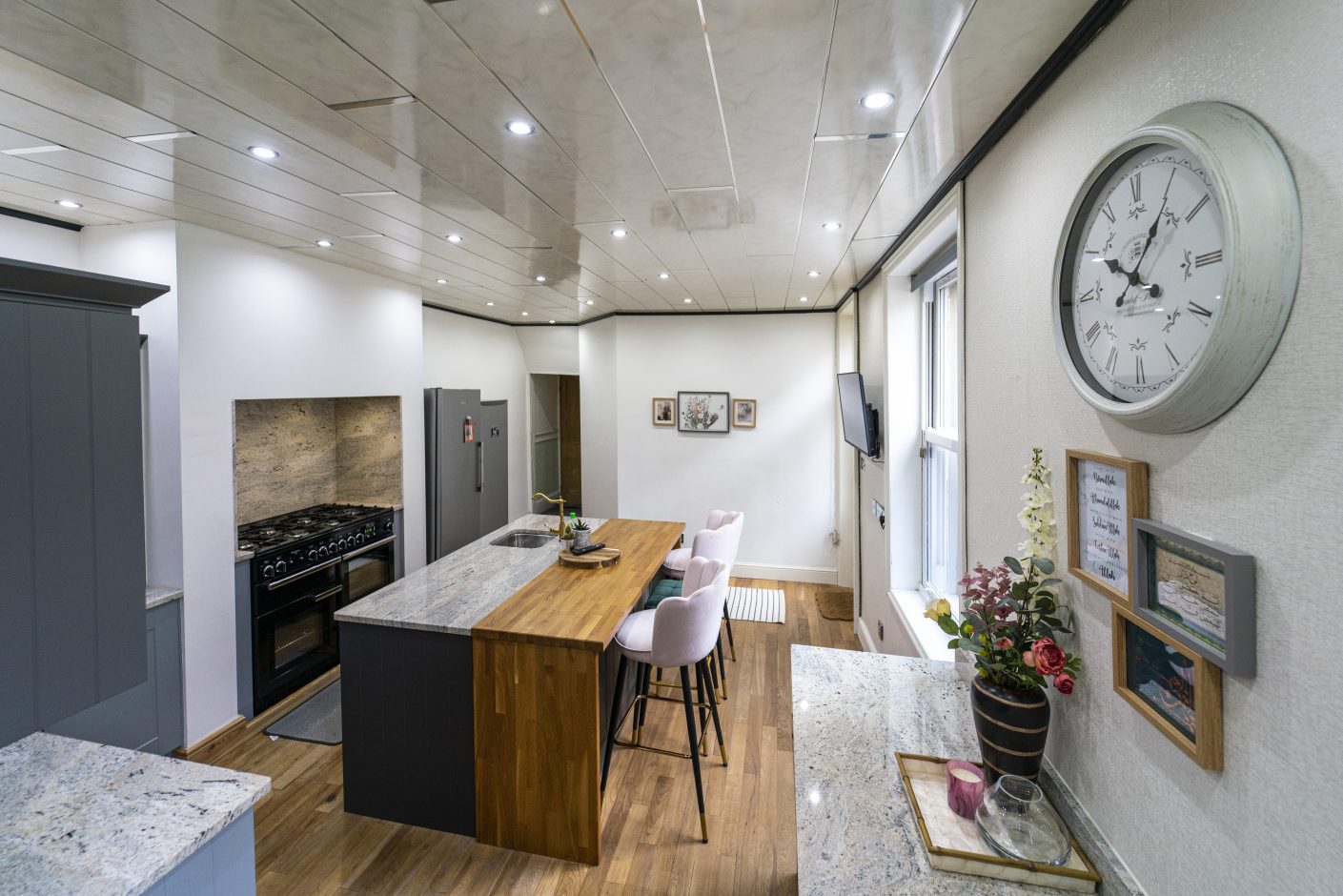 Angled wide shot of an Ivory Fantasy Granite island worktop with timber breakfast bar section, showing the island length, seating and natural light from doors and skylights.