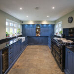 Wide perspective down a blue kitchen with Absolute Black Granite worktops on both sides, showing the sink run and cooking area at the far end.