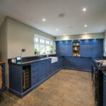 Full kitchen view with blue cabinetry and Absolute Black Granite worktops along the perimeter run, showing the sink area and a drinks fridge under the worktop.