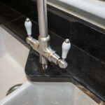 Close up of a kitchen tap over a sink with Absolute Black Granite worktop and matching Granite upstand, showing the polished finish around the corner.