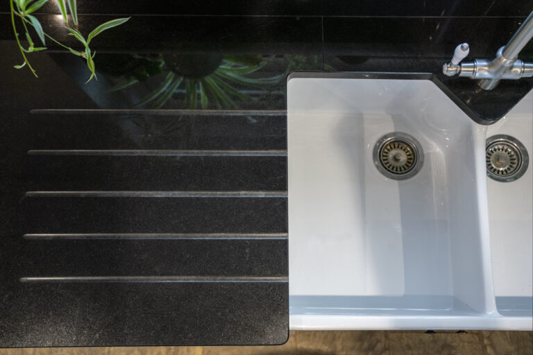 Close up of Absolute Black Granite worktop with precision cut drainer grooves next to a white sink, showing the polished finish and clean lines.