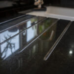 Close up of Absolute Black Granite worktop showing precision cut drainer grooves with reflections on the polished surface near the sink.