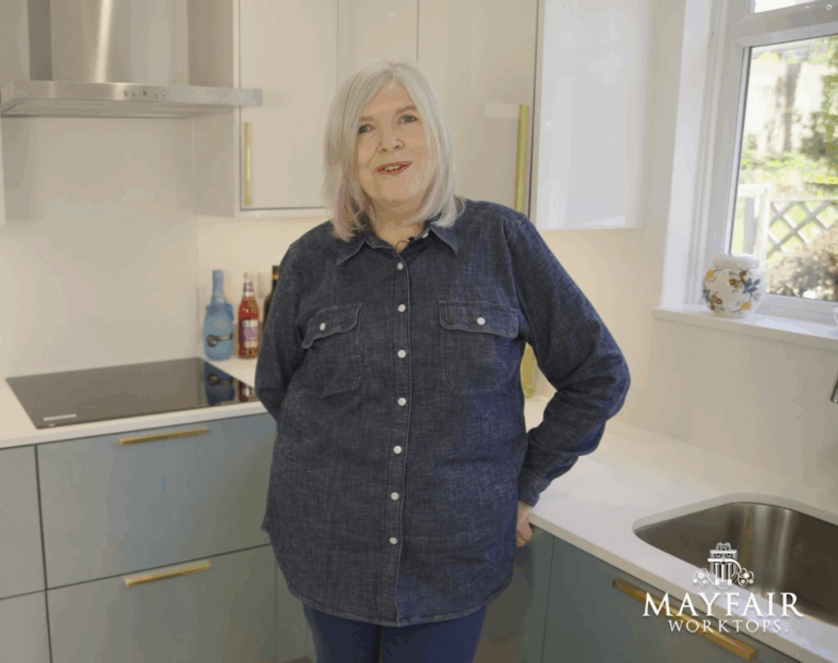 Anita in her kitchen with Dover White Quartz worktops visible around the sink and corner run