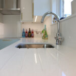 Close-up of Dover White Quartz drainer grooves beside a stainless steel sink and chrome tap