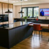 Open plan kitchen view with an Absolute Black Granite island and breakfast bar seating, showing pendant lights, sink area and large windows.