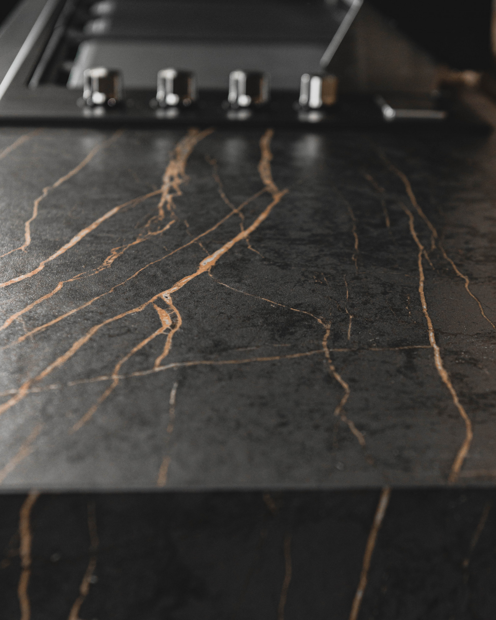 Laurent Porcelain worktop close-up showing dark stone-effect surface with strong gold veining under kitchen lighting.