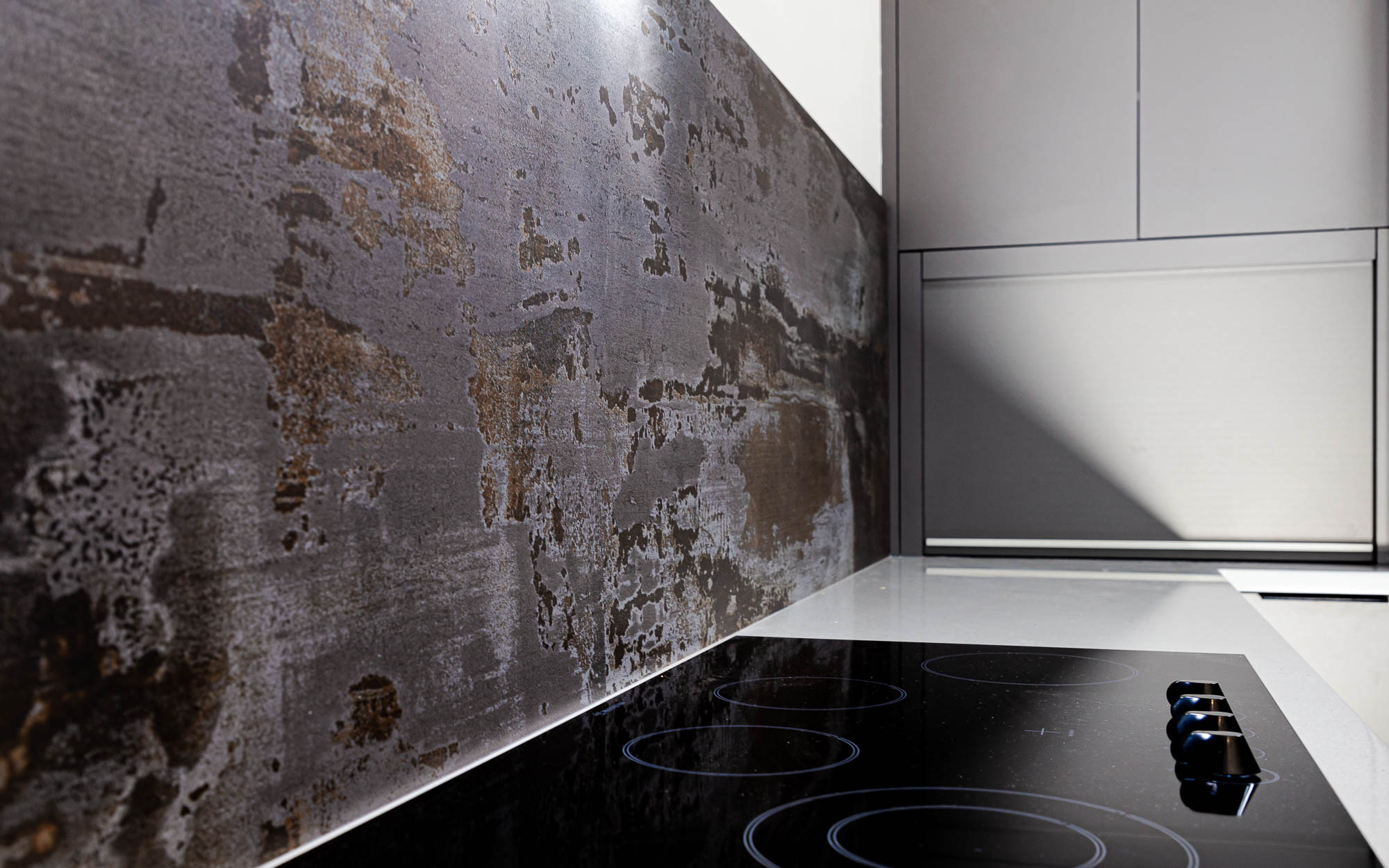 Trilium Porcelain splashback panel behind a ceramic hob with a worktop edge and light wall return visible on the right