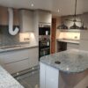 Modern kitchen view with Azul Platino Granite worktops, showing a curved island with a polished light grey speckled Granite surface and pendant lighting.