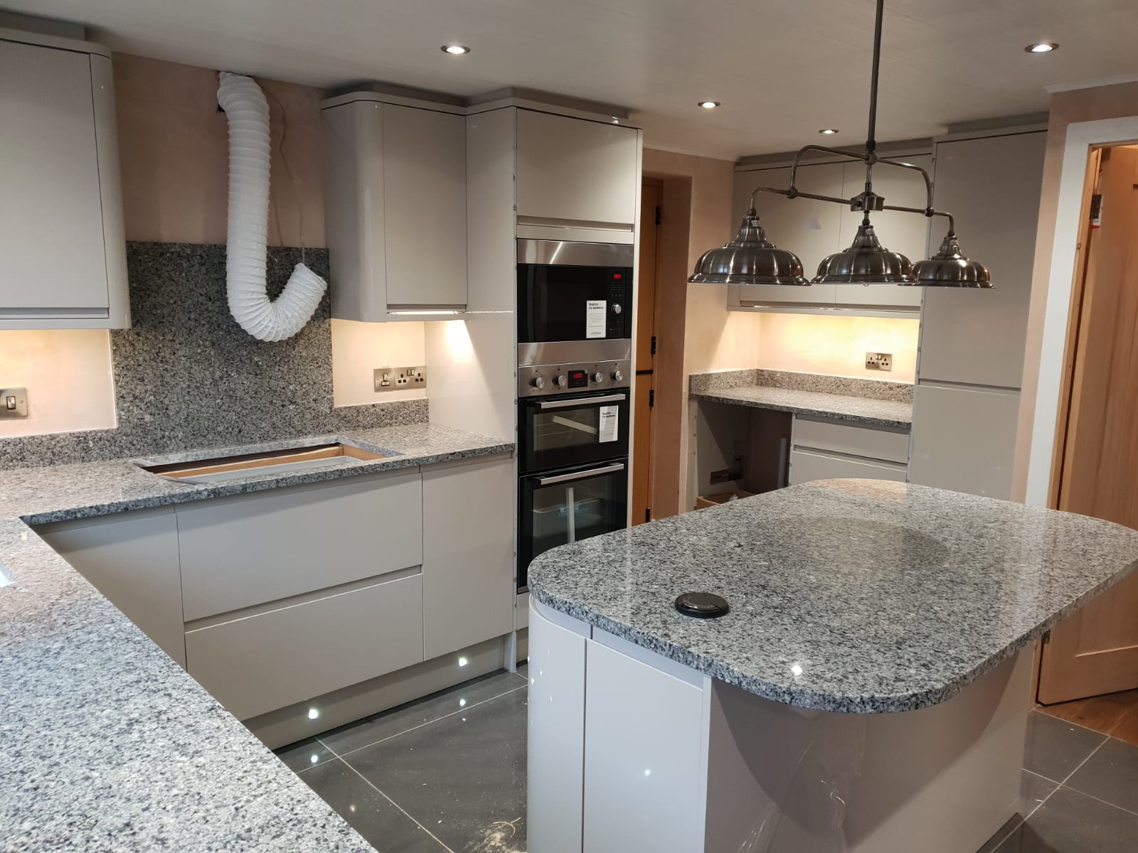 Modern kitchen view with Azul Platino Granite worktops, showing a curved island with a polished light grey speckled Granite surface and pendant lighting.