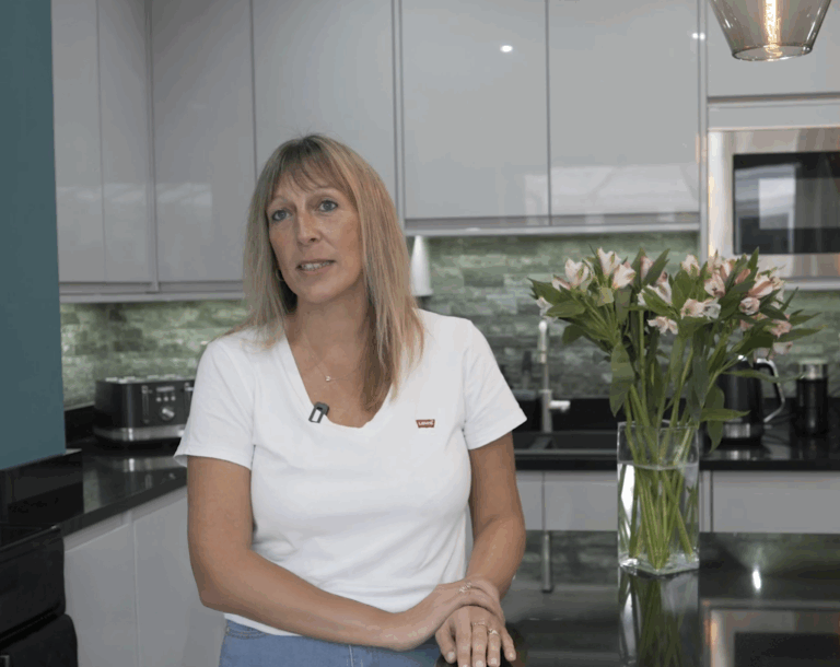 Testimonial still of a customer speaking on camera in a fitted kitchen after an Absolute Black Granite worktop installation by Mayfair Worktops.