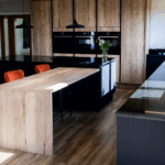 Wide kitchen view showing an Absolute Black Granite island worktop with a long breakfast bar and timber cabinetry, with pendant lights and seating.
