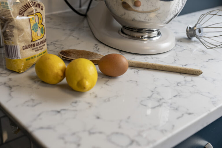 Close-up of Arabescato Quartz worktop edge with lemons and a wooden spoon showing grey veining on a white surface