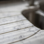 Close-up of Arabescato Quartz drainer grooves beside a sink showing grey veining across the surface
