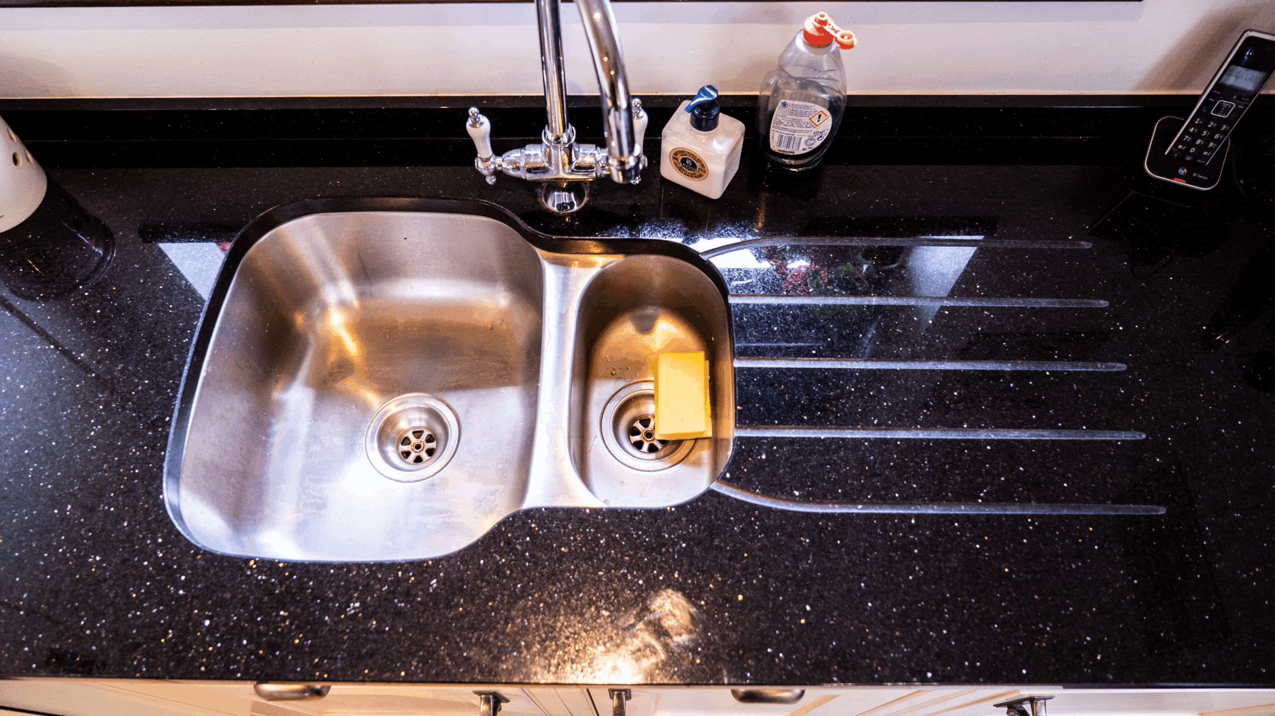 Sink area in Star Galaxy Granite with drainer grooves and a polished finish, showing the sparkling fleck pattern beside a stainless steel sink.