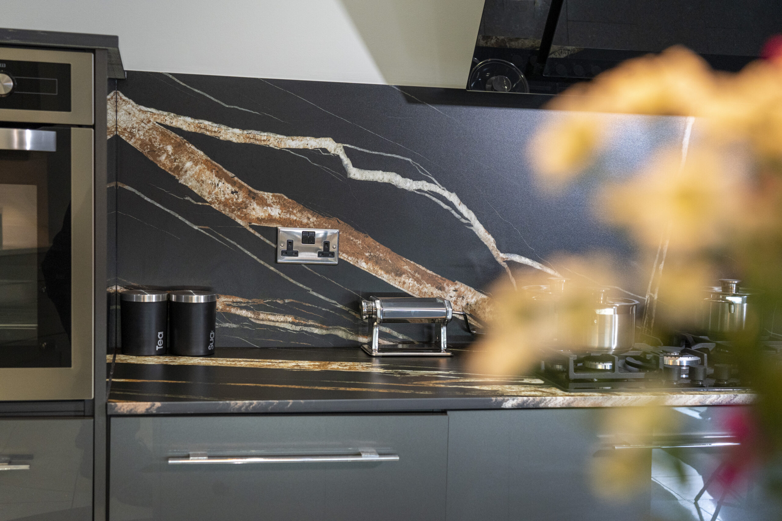 Noir St Laurent Porcelain worktop and splashback installed with bold gold and copper veining, shown above grey kitchen units with a socket on the wall.