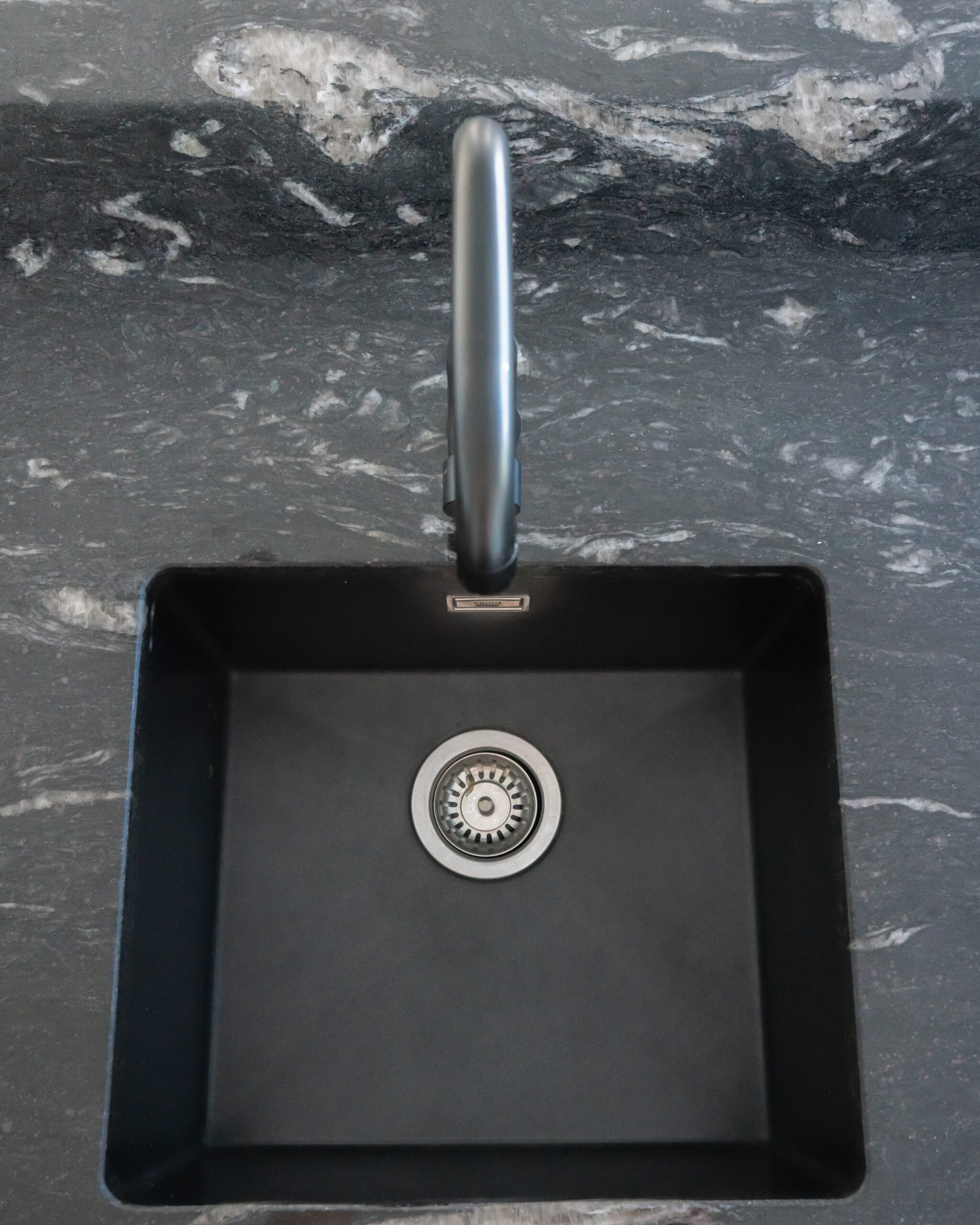 Overhead view of an undermount sink set into Cosmic Black Granite, showing the polished Granite surface and tap positioned above the bowl.