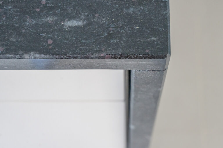 Close up of a Cosmic Black Granite worktop corner showing the polished edge profile and waterfall end detail above white cabinetry.