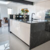 Side view of a modern kitchen with Cosmic Black Granite worktops on the island and perimeter run, showing waterfall ends and a polished surface finish.